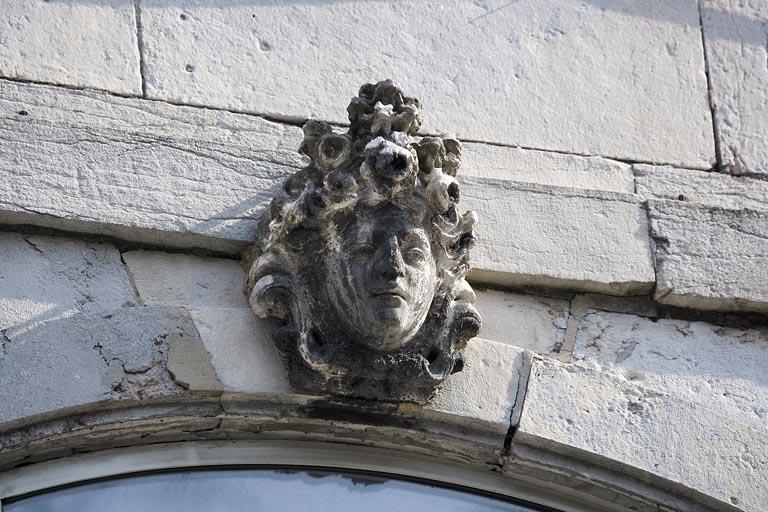 Détail de la clé d'une fenêtre au premier étage sur rue : figure coiffée d'un amas de fleurs.