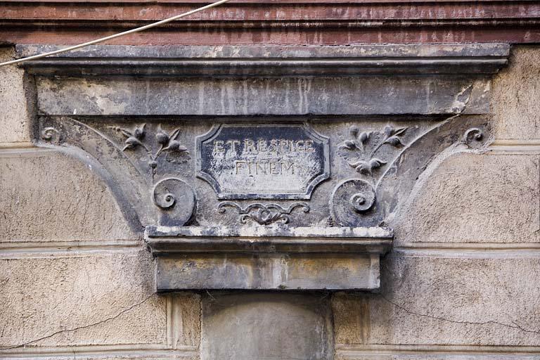 Détail du chapiteau du portique portant l'inscription latine 'et considère la fin'.