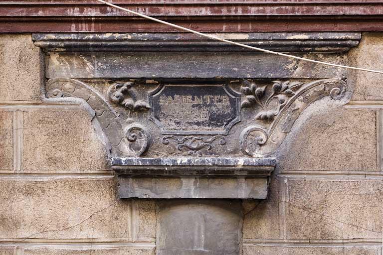 Détail du chapiteau du portique portant l'inscription latine 'agis sagement'.