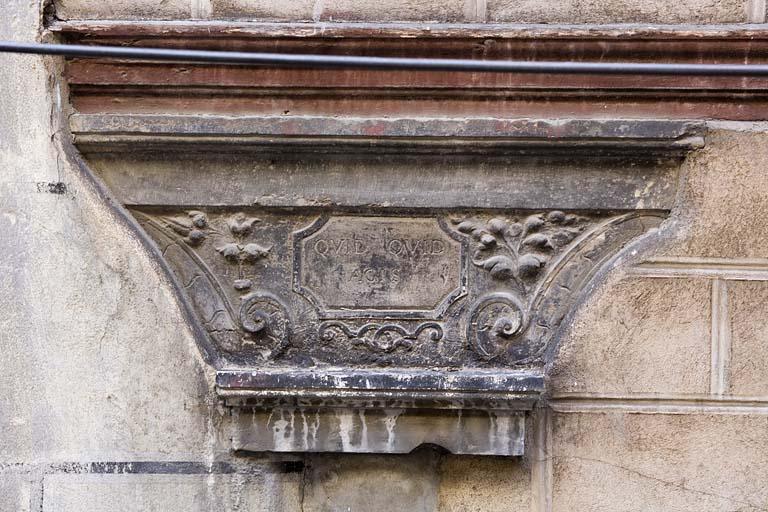 Détail du chapiteau du portique portant l'inscription latine 'quoique tu fasses'.