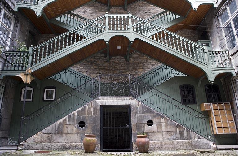 Escalier à cage ouverte à droite de la première cour : vue d'ensemble, de face, des premières volées en maçonnerie.