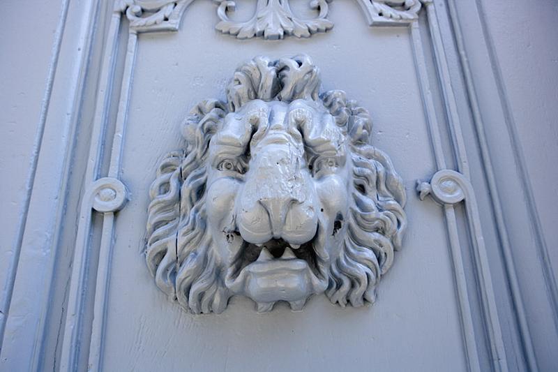 Logis principal : détail d'une tête de lion décorant un des vantaux du portail d'entrée.