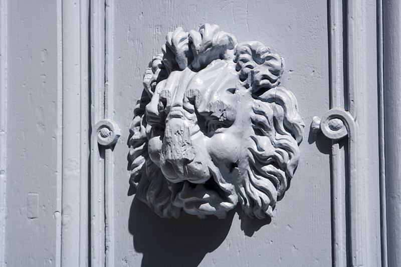 Logis principal : détail d'une tête de lion sur l'un des vantaux du portail d'entrée : de trois quarts.