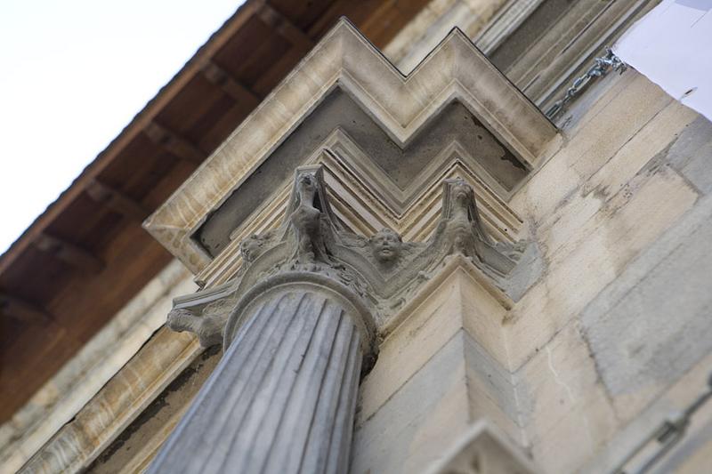 Façade principale : détail du chapiteau d'une colonne encadrant le portail d'entrée, vue rapprochée.