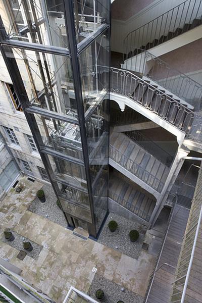 Vue d'ensemble de l'escalierà cage ouverte sur cour et de l'ascenseur.