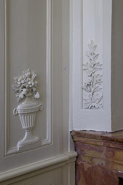 Intérieur, chambre à gauche du salon : lambris, détail d'un pot à fleurs et d'un motif végétal.