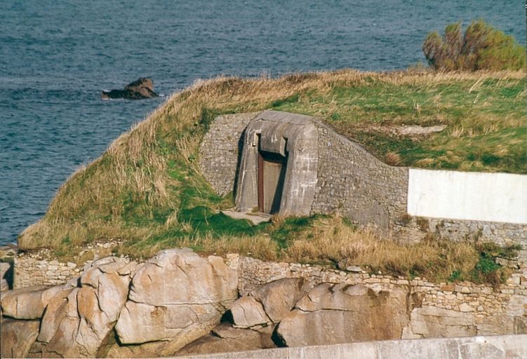 Vue du bunker - casemate de type 611 flanqué de murs en maçonnerie de moellon de granite (état en 2002) ; Vue générale depuis le sud-ouest (état en 2002). L'embrasure du bunker est flanquée de murs en maçonnerie de moellon de granite. Une portion de ce mur est enduite et peinte en blanc car servant à la signalisation maritime