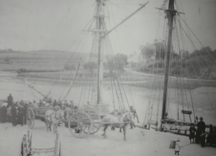 Déchargement d'une goélette de cabotage au mât de charge avec transport ensuite en charrette ; Déchargement au mât de charge d'un navire goélette armée au cabotage devant les quais de Dahouët