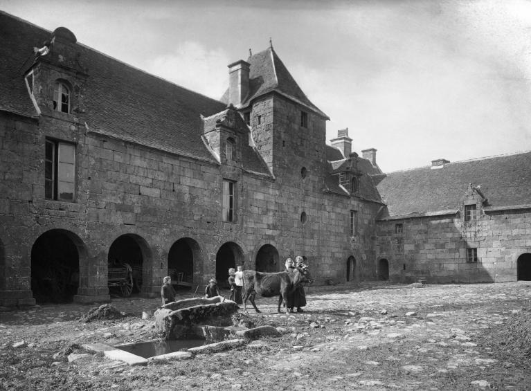 Plouaret, Guernanchanay : fontaine et auge situées au milieu de la cour du manoir, femme et enfants avec une vache, photographie vers 1862-1914 (source : fonds photographique Villard)