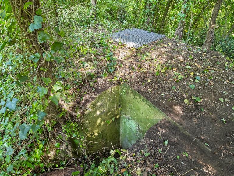 Vue générale du côté de l'entrée située au Nord. L'entrée est murée par des parpings ; une grille protège les visiteurs d'une chute dans le poste d'observation ; Vue du bunker - poste d'observation et de tir de type 58c dit Tobruk-Stand implanté au Sud près du bunker - casemate de type 680. Son entrée est murée par des parpaings. Une grille protège le poste d'observation et de tir circulaire des risques de chute