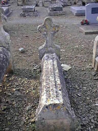 Vue d'un tombeau en bâtière applanie ornée d'une croix très allongée avec stèle ornée d'une croix.