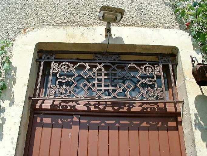 Logis, élévation antérieure, porte d'entrée, détail de la grille en fonte protégeant l'imposte vitrée.