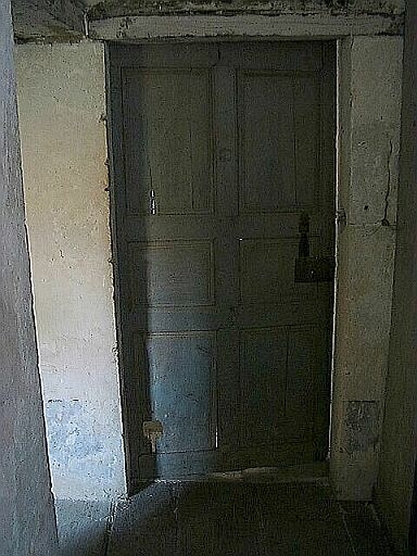 Logis, étage, couloir pratiqué du côté est par les cloisons en bois des chambres, porte à panneaux de communication.