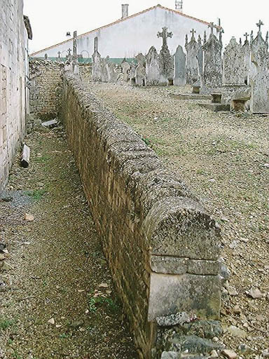 Muret de séparation entre l'église et le cimetière ; à remarquer la réutilisation des tronçons de couvercles de sarcophage en chaperon.