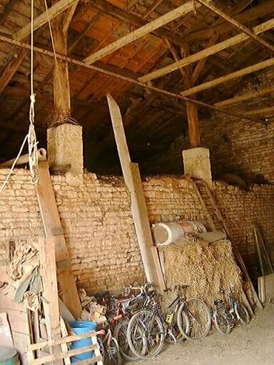 Dépendances, grange bâtie entre les deux logements, intérieur, vue vers le muret de séparation des étables et des piles en pierre supportant la charpente.