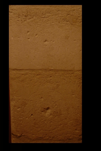 Logis, rez-de-chaussée, montant commun au deux portes de communication entre l'escalier à vis, la pièce principale et l'autre partie du logis, détail des pierres avec des graffitis de cercles.