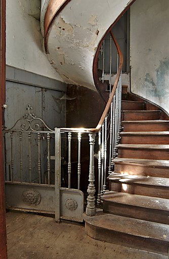 Logis : vue de l'escalier tournant en charpente et fonte donnant accès à la cave et aux étages d'habitation.