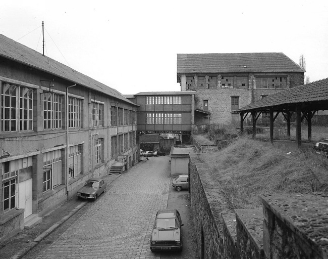 A gauche les bureaux et magasins de l'usine de chaussures (ateliers de décoration de 1853, atelier de tournage et moulage en 1893), au centre la passerelle reliant les parties est et ouest de l'usine, à droite un magasin industriel (ancienne salle des machines).