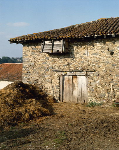 Grange-étable. Elévation sud. Détail de la porte d'étable, au linteau en bois protégé par un bandeau de pierres saillantes et de la boite à pigeons accrochée sous le toit.