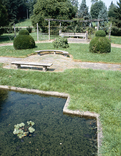 Vue partielle de la roseraie. Pièce d'eau en premier plan, bancs et pergola en arrière-plan.