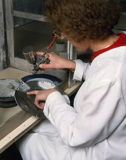 Technique du décor exécuté à l'émail en 'blanc relief'. Positionnement du cache en étain sur l'assiette en porcelaine et vaporisation du 'blanc relief'.