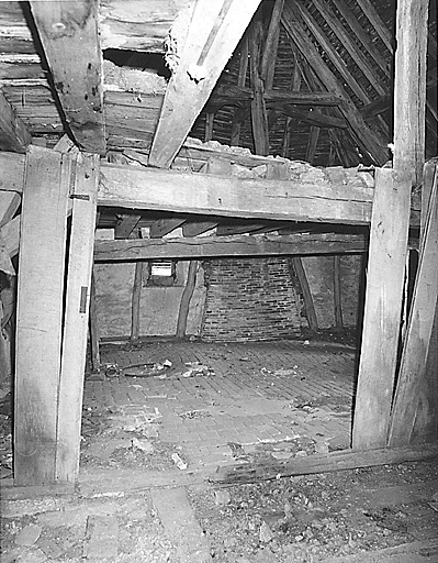Logis. Vue partielle de l'étage de comble, partie sud-est avec sol pavé de carreaux en terre cuite ; au fond, conduit de cheminée contre mur sud.