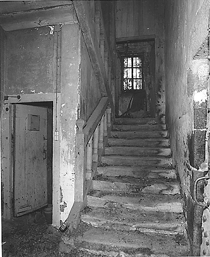 Intérieur. Vue de la première volée de l'escalier en bois, tournant, à retours et sans jour, avec rampe ornée de balustres ronds.