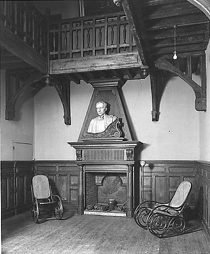 Hall. Vue partielle montrant la cheminée en bois dont la hotte est décorée du buste en plâtre de François Chénieux et la galerie en bois courant au niveau de l'étage.