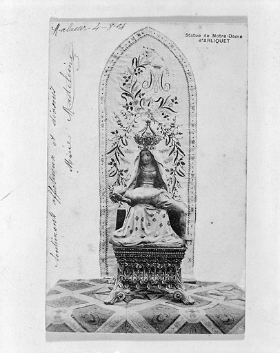 Vue du groupe sculpté représentant Notre-Dame-d'Arliquet, ornée de la couronne. Groupe reposant sur un socle et placé devant une tenture brodée portant le monogramme de la Vierge.