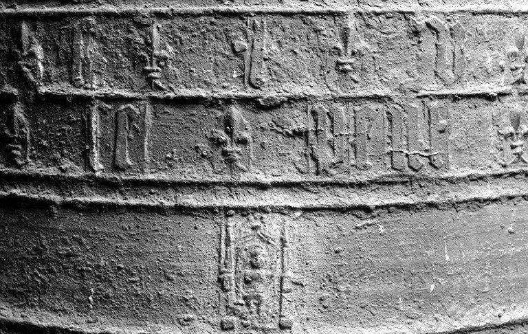 Vue de détail d'une petite partie de l'inscription, d'un motif représentant l'Ecce Homo sous une arcade à pinacles latéraux et de la frise inférieure moulurée ornée d'un décor végétal.