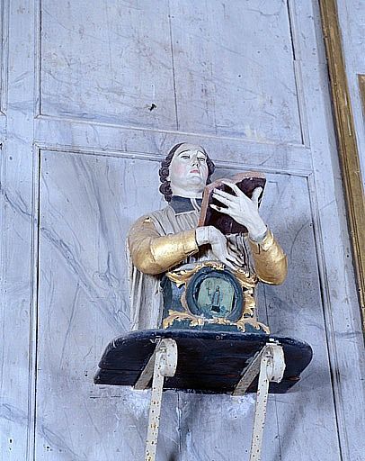 Vue rapprochée du buste-reliquaire fixé en haut à gauche du retable : saint prêtre tenant un livre saint.