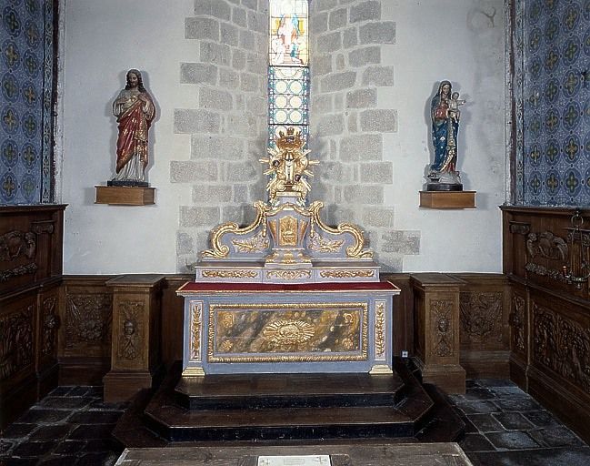 Vue du mur est du choeur : autel surmonté d'un gradin, sur lequel est posé le tabernacle à exposition, entre des lambris bas avec piédestaux de chaque côté de l'autel.