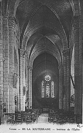 Vue de l'intérieur de l'église depuis le bas de la nef. Vue permettant de discerner du mobilier et des objets religieux aujourd'hui disparus (ancien maître autel, clôture de choeur, statue de Vierge, chemin de croix).