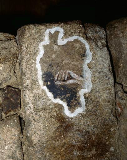 Fragment de peinture représentant une main situé sur une pierre remployée dans un bloc de maçonnerie servant d'étai dans le déambulatoire nord de la crypte.