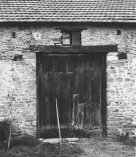 Grange-étable (Mortorat, cad. 1992, C1 828). Détail d'un 'portanet' : petite porte piétonne découpée dans un vantail de la porte charretière. Ici, le portanet est surélevé au-dessus d'une planche de seuil pour empêcher les poulets de s'échapper.