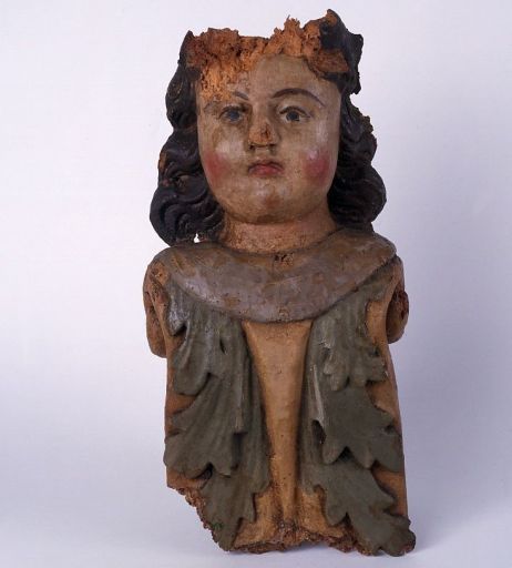 Détail : figure d'applique, vue de face. Angelot polychrome provenant du retable du maître-autel, découvert après restauration. Il était vraisemblablement appliqué sur un des stylobates supportant les colonnes du retable. Il est aujourd'hui conservé dans une vitrine du musée.