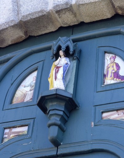 Portail ouest orné de 18 plaques de porcelaine enchâssées dans la menuiserie des vantaux. Détail des 4 plaques centrales et de la statuette de Vierge en porcelaine.