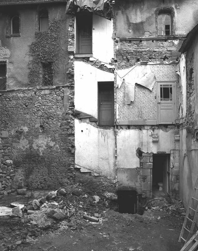 Vue partielle de l'élévation ouest donnant sur la cour accessible par la rue Détournée, depuis la démolition du bâtiment au toit formant terrasse et de la tour en brique qui abritait un escalier ; cette vue montre l'accès à la cave et une porte du rez-de-chaussée aux piédroits moulurés, surmontée de deux corbeaux.