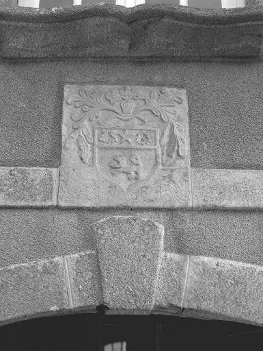 Elévation antérieure donnant sur la cour. Vue de détail d'une pierre sculptée qui agrémente le bandeau, au-dessus de la porte ; elle représente un blason non identifié et porte la date '1784 '.