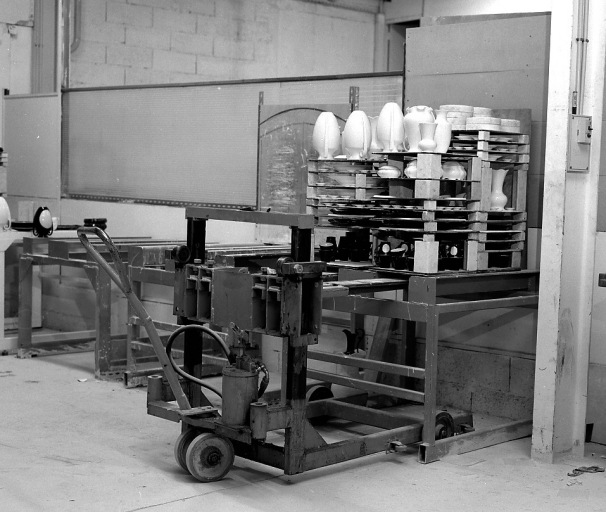 Une fournée de pièces de porcelaine après cuisson et le chariot élévateur hydraulique permettant les opérations d'enfournement et défournement. On distingue sur le côté le tracé d'un gabarit permettant la préparation des pièces de porcelaine avant l'enfournement.