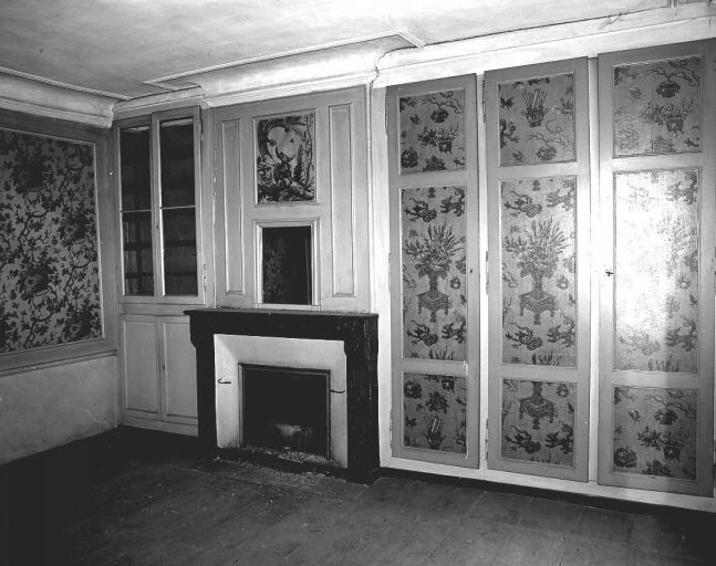 Premier étage. Vue d'une pièce ornée de papier peint aux motifs floraux (corbeilles et bouquets de fleurs) et d'une scène exotique, dans le trumeau de la cheminée (personnage debout sur un char à voiles).