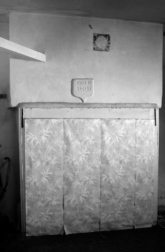 Rez-de-chaussée, pièce donnant sur la cour (ancienne cuisine?). Vue de la cheminée en pierre dont la hotte est ornée d'un écu portant l'inscription gravée : ' M G II / 1608'.