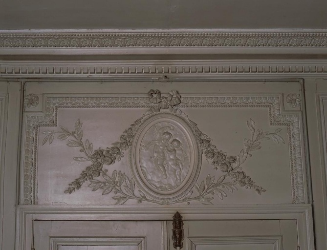 Intérieur, rez-de-chaussée, salon. Porte à deux vantaux. Vue de détail du dessus de porte et de son décor sculpté comportant un médaillon orné de deux angelots.