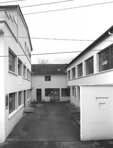 La cour de l'usine : à gauche les bâtiments construits à partir de 1966 ; au fond, le bâtiment qui abritait le four rond de 1906 puis les premiers fours-cellules au gaz (le four rond se situait derrière la porte vitrée actuelle), ainsi que les ateliers d'émaillage, peinture, useurs de grains, modelage... ; à droite les anciens magasins, bureaux et bûcher (rez-de-chaussée), et les ateliers de coulage (étage).
