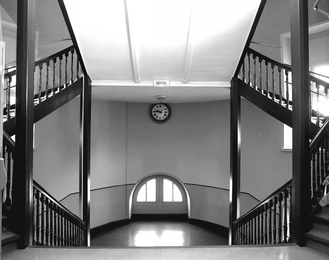 Les escaliers distribuant les ateliers des ailes nord et sud : vue prise depuis le palier du 1er étage, en direction du repos. On distingue l'horloge de l'usine, à double cadran, intérieur et extérieur.