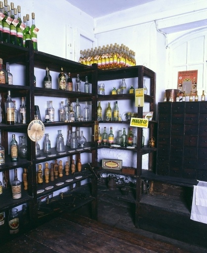 Vue des étagères où était stockée la production de la distillerie mise en bouteilles. Partiellement utilisées pour le stockage, ces étagères servent aujourd'hui pour l'exposition de bouteilles anciennes et d'objets publicitaires (apéritifs 'La Sève Centrale' et 'Panazô').