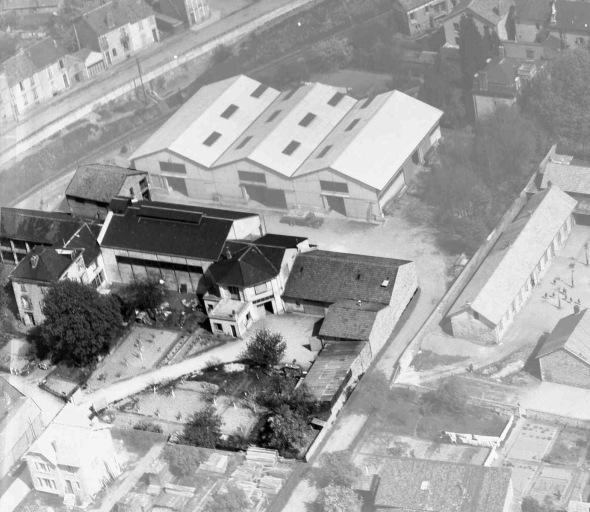 Vue aérienne du site en 1953, prise du sud-ouest. De gauche à droite : un atelier de décoration et de fabrication de l'usine de porcelaine, une habitation (perpendiculaire), les silos de la Semeuse du Centre construits en 1946 (bâtiment coiffé d'un lanterneau), l'ancien bâtiment du four (façade antérieure polygonale), le chai de M. Lajudie de 1943. A l'arrière, les dépôts de la Semeuse du Centre construits en 1950.