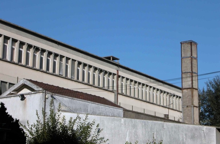 La toiture de l'ancien bâtiment du four rond au mazout (deux pans en tuile mécanique) et une ancienne cheminée de l'usine.