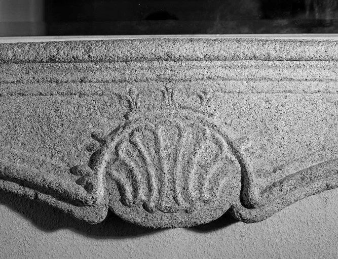 Premier étage. Cheminée en granite de style 18e, présentant un manteau à mouluration chantournée, orné d'une coquille sculptée et des piédroits galbés. Vue de détail du décor de coquille.