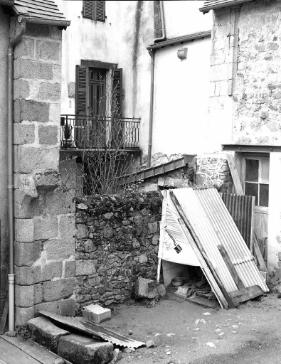 Vue partielle, depuis la cour de la maison voisine située au n° 21, de l'élévation postérieure, remontée fin 19e ou début 20e siècle, après démolition d'une partie est de la maison. Cette vue montre des vestiges architecturaux concernant cette partie démolie (corbeau de poutre de rive et piédroit de baie), aujourd'hui inclus dans le gros oeuvre du bâtiment situé à droite (bâtiment ayant abrité une forge au début du siècle) ; la partie du mur de ce bâtiment situé à gauche du piédroit correspond à l'épaisseur de l'élévation postérieure initiale de la maison étudiée. Cette vue montre également à gauche l' arrachement d'une arcade accolée à cette ancienne élévation (vestige d'une ancien portail donnant accès à une cour ?).